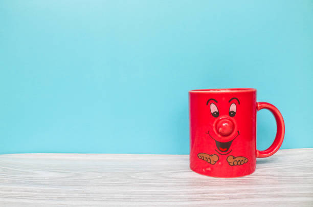A red cup with a cute face isolated on a blue background. Red mug wallpaper isolated with space for text.