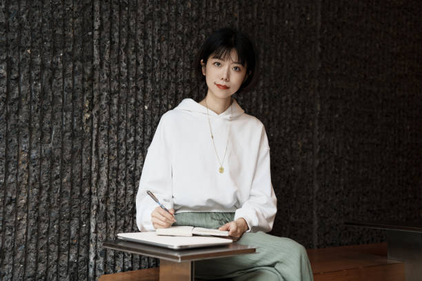 An Asian woman working in an outdoor cafe writes with a notebook