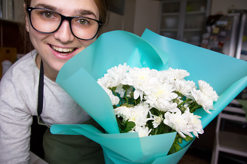 Florist woman smiling holding bouquet with white daisies. Arranging a bouquet of beautiful colorful flowers. Blue background. Out of focus.