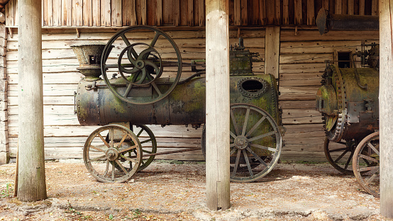 Vintage Richard Garrett and Sons, made in UK, mobile steam engine with a furnace and a boiler in which water is turned into steam, near a wooden planks wall background.