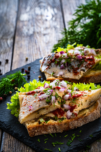 Tasty sandwiches - toasted bread with pickled herrings and red onion on wooden background