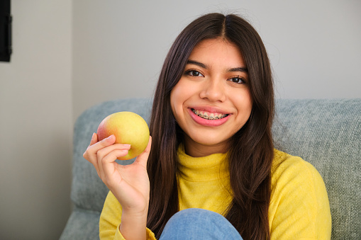 Female smiling teenager with braces and an apple at home.