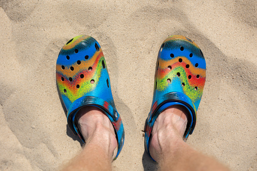 Ukraine, Kyiv - July 04. 2022: Legs in colorful crocs footwear on the beach, copy space for text. olorful trendy beach shoes. Summer vacation concept.
