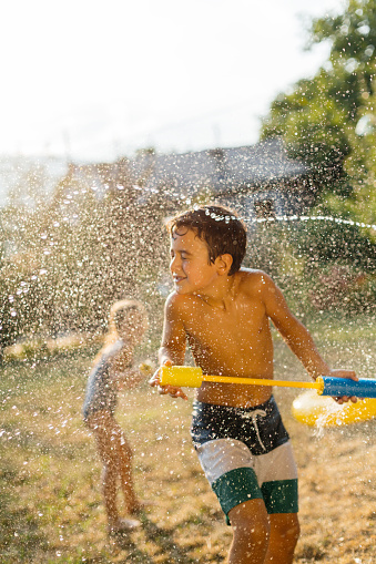 Cheerful boy having fun with squirt gun and water fight on a hot summer day