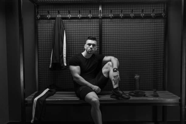 Black and white shot of handsome young man sitting on the bench in gym dressing room