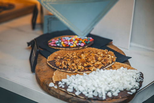 A tantalizing display awaits at a Stroopwafel candy store in Amsterdam, Netherlands, showcasing a wide assortment of cookies adorned with rich chocolate. The decadent treats, including traditional Stroopwafels filled with caramel syrup, are beautifully presented, enticing passersby to indulge in the irresistible delights of Dutch confectionery. This image captures the essence of sweet temptation and culinary craftsmanship found in the heart of Amsterdam's vibrant streets