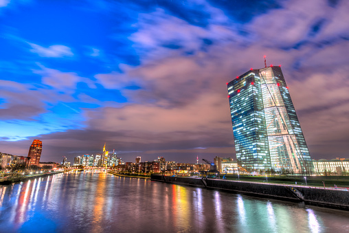The ECB (European Central Bank) in Frankfurt am Main at dusk in the evening with artificial lighting and the skyline in the background and the River Main in the foreground