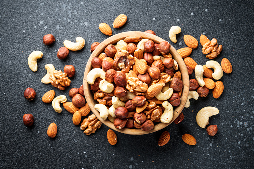 Nuts assortment at black background. Almond, hazelnut, cashew in wooden bowl.