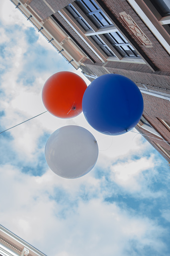 A festive scene unfolds in Amsterdam, Netherlands, as vibrant red, white, and blue balloons fill the air, mirroring the colors of the Dutch flag, during Kings Day celebrations. The cheerful atmosphere and patriotic display capture the spirit of this national holiday, where locals and visitors come together to honor the Dutch monarchy with lively festivities and colorful decorations. This image epitomizes the joyous energy and pride felt throughout the city during Kings Day.