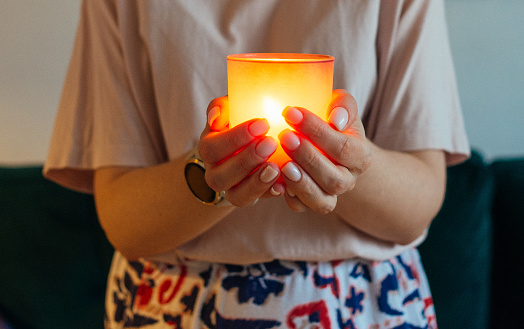 Close-up image of a candle glowing in woman's hands, evoking a sense of warmth, relaxation, and tranquility