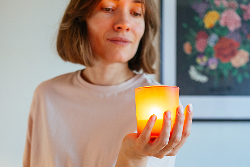Close-up image of a candle glowing in woman's hand, evoking a sense of warmth, relaxation, and tranquility. Selective focus is on the candle