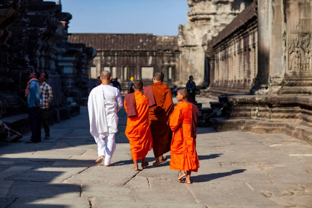 Contemplative Cambodian monk in an orange robe sits on the ancient steps of a temple ruin lost in thought looking at ancient carvings, Siem Reap, Cambodia, Asia