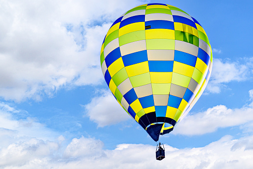 Colorful hot air balloon flying over blue sky with white clouds