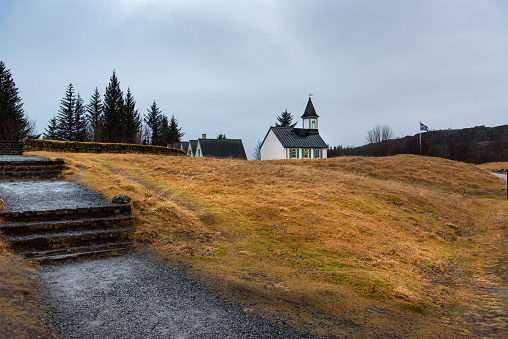 Experience the picturesque beauty of thingvellir national park in iceland as a charming church stands atop a hill surrounded by trees and a serene winter landscape