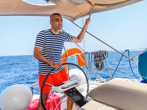 Portrait of a young brunette man driving a boat with a smile, learning to navigate.