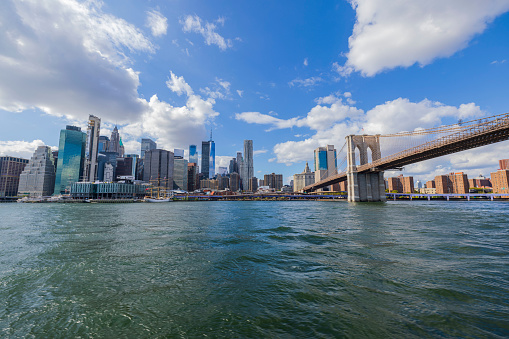 Beautiful view from Hudson River of Brooklyn Bridge and skyscrapers of Manhattan against backdrop of blue sky with white clouds. NY. USA.