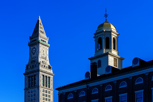 Boston, Massachusetts, USA - February 20, 2024: View of the Custom House Tower and the cupola atop the Faneuil Hall building. The Custom House in Boston was established in the 17th century and stood near the waterfront. A tower was added in 1915; the building joined the National Register of Historic Places in 1973 and was designated a Boston Landmark in 1986. Faneuil Hall is a marketplace and meeting hall located near the waterfront and today's Government Center, in Boston. Opened in 1742, it was the site of several speeches by Samuel Adams, James Otis, and others encouraging independence from Great Britain. It is now part of Boston National Historical Park and a well-known stop on the Freedom Trail.