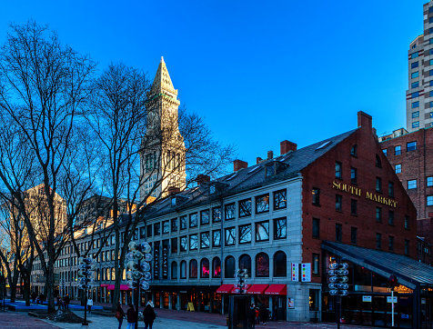 Boston, Massachusetts, USA - February 20, 2024: View of the South Market building of the Quincy Market site in downtown Boston. Quincy Market includes Faneuil Hall flanked by the North and South Market buildings. It was constructed between 1824 and 1826 and named in honor of mayor Josiah Quincy, who organized its construction without any tax or debt. It is now part of Boston National Historical Park and a well-known stop on the Freedom Trail. The Custom House Tower (c. 1837-1847) is in the background.