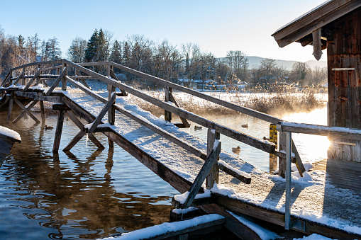 Wooden bridge at Frozen Lake Staffelsee  in winter on a sunny afternoon at Seehausen, Bavaria, Germany