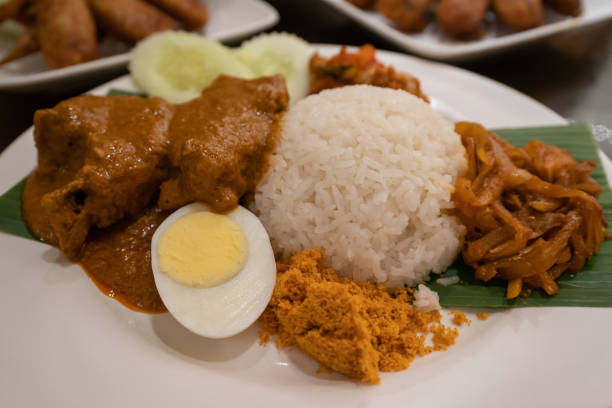 Asian food Nasi Lemak is a rice dish infused with coconut milk. Served with sambal, curry chicken ,cucumber, boiled egg with curry sauce and etc. stock photo
