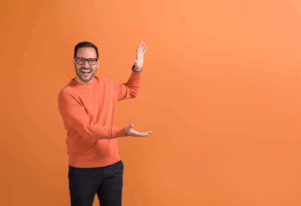 istock Cheerful young salesman presenting new product with empty hands while standing on orange background 2037826954