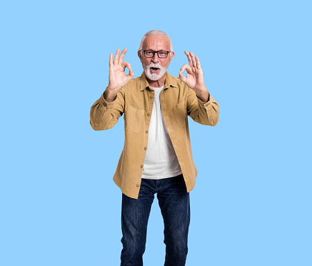 Portrait of senior male entrepreneur showing OK signs and screaming cheerfully on blue background