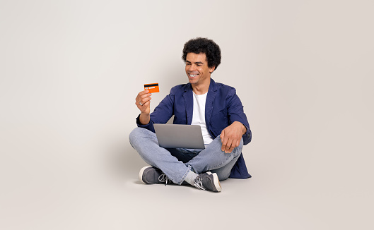 Smiling businessman shopping online with credit card and netbook while sitting on white background