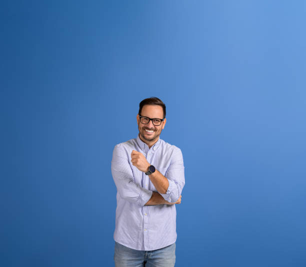 istock Portrait of handsome young manager in eyeglasses smiling at camera while standing on blue background 2037832782