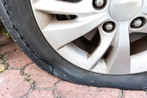 Closeup of deflated flat car tire with rupture at the side of the wheel