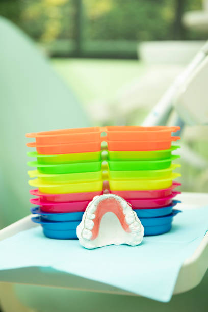 Group of colored boxes and a top acrylic retainer on a white plaster model on a tray in a dental office.