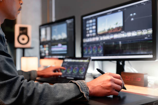 filmeur, monteur vidéo ou coloriste, vêtu d’une veste en jean, travaillant avec des séquences ou des vidéos sur son ordinateur personnel à l’aide d’un stylo et d’une tablette, dans son studio de création. - studio de post production photos et images de collection