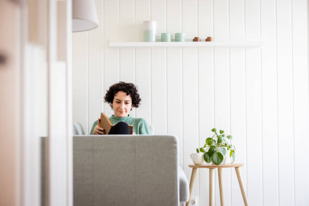 istock Young lady is reading a book on sofa in living room. 2037859337