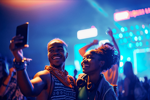 Happy African American couple having fun and taking selfie during summer music festival at night.