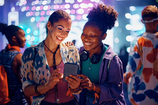 Young happy woman taking selfie while attending live performance during summer music festival at night.