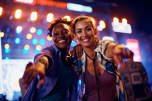 Happy female friends having fun on summer music festival at night and looking at camera.