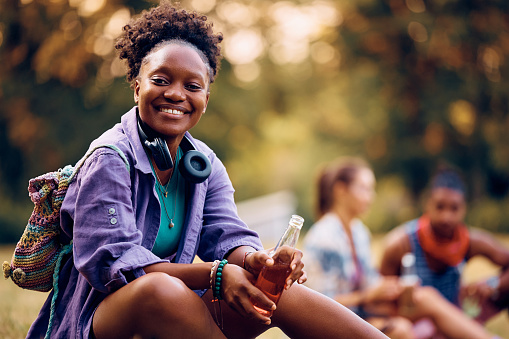 Happy African American woman waiting for open air music concert in nature and looking at camera.
