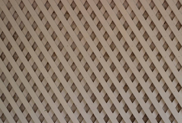 A criss-crossing white trellis or lattice made of thin strips of white painted wood, sat against a whitewashed brick background and filling the frame.
