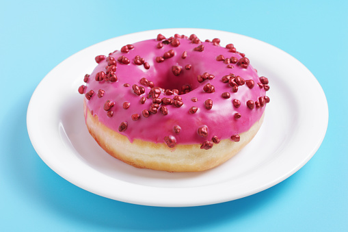 Pink donut in plate on blue background. Sweet glazed dessert