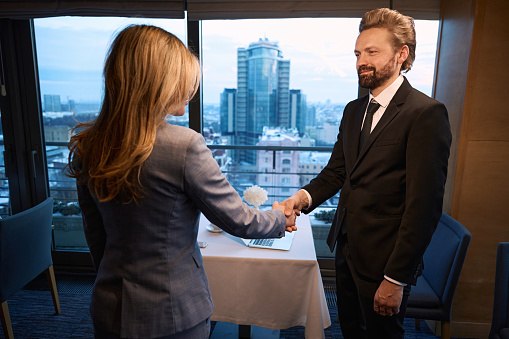 Elegant businessman shaking hands with a woman, cityscape outside the window