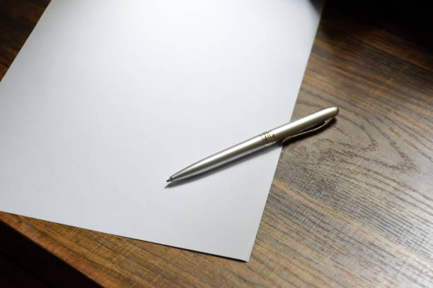 Aluminium pen and blank paper are placed on a wooden patterned desk for take notes or work at office.