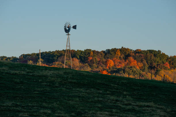 Blue sky behind a hill of colorful fall autumn folliage with an Amish windmill on an October morning. Walnut Creek, Ohio in Holmes County. Green, old-fashioned energy.