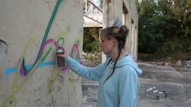 Female artist draws colorful graffiti on the wall and creates her art