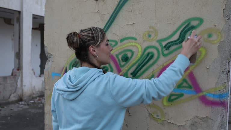 Female street artist draws colorful graffiti on the wall, using sprays