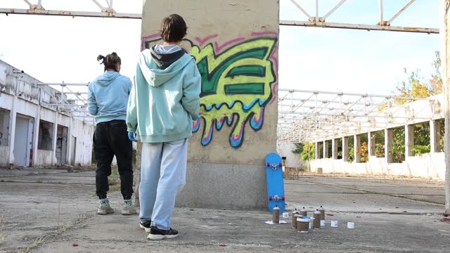 Rear view of two best friends drawing graffiti and creating their art