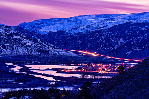 Confluence of Eagle and Colorado Rivers - Scenic night dusk view with the town of Dotsero, Colorado situated along the Eagle River and Colorado River with Interstate 70 running through Glenwood Canyon. Night view with town glowing and long exposure light trails from vehicles on road. Scenic snowcapped mountains in background with pink sky and reflections in water.