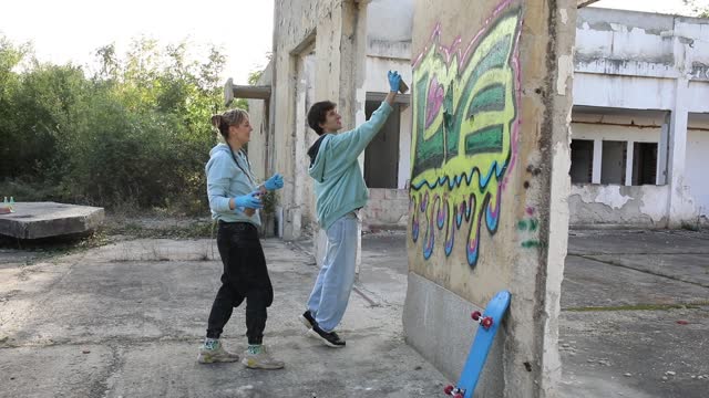 Two young street artists wear gloves as they draw graffiti on the wall of an abandoned building