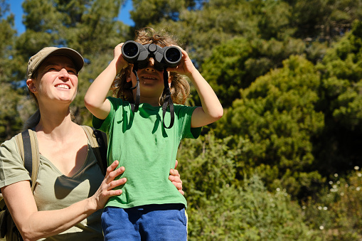 Mother and son using binoculars in nature, looking up