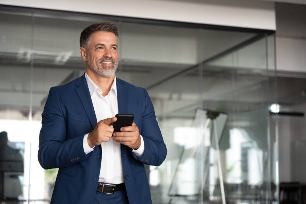 istock Smiling middle age entrepreneur using cell phone mobile app, looking aside. Digital technology application and solutions for business. Mature 40s businessman wearing suit holding smartphone indoors. 2038078639