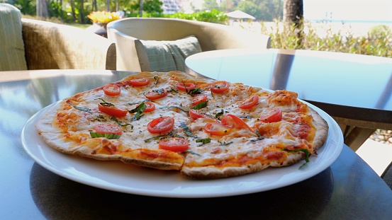 A delicious California style pizza with melted pizza cheese is served on a white plate resting on a table.
