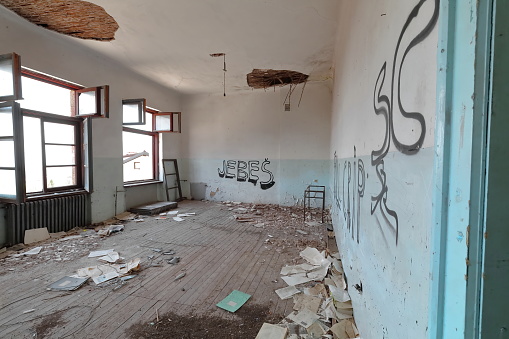 Old classroom inside the remains of a ruined, abandoned former primary school built in AD 1948 full of rubble with broken windows, graffiti and peeling walls and ceilings. Vevcani-North Macedonia.
